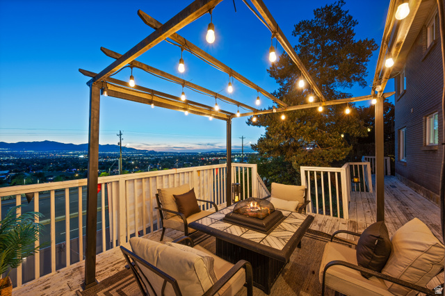 9750 Indian Ridge Drive Sandy, UT 84092 - Photo 18 of 40 Expansive outdoor deck featuring a wooden pergola with string lighting, white railing, and a built-in fire pit table
