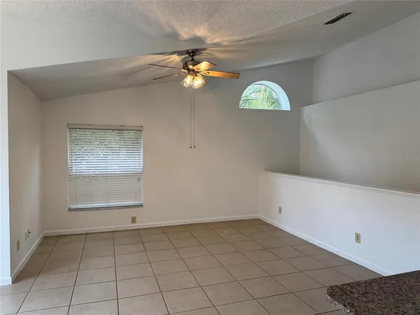a view of an empty room with window and chandelier fan