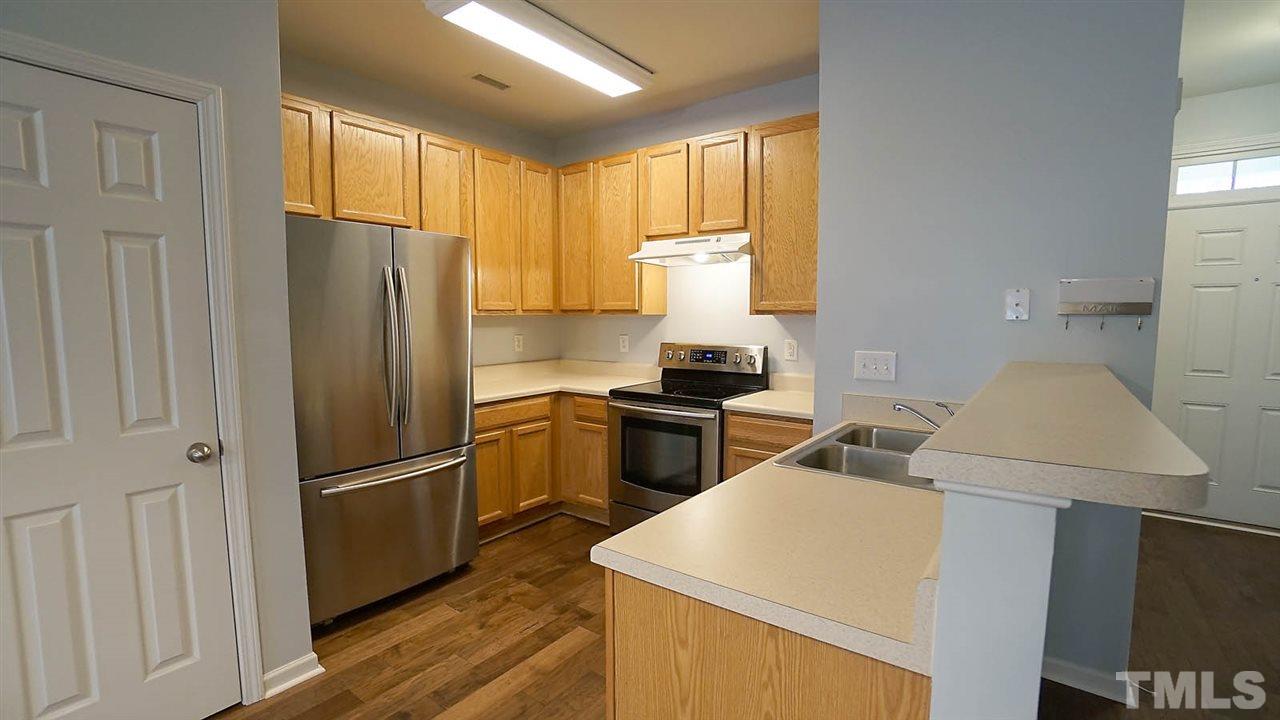 8311 Martello Lane Raleigh, NC 27613 - Photo 4 of 30 a kitchen with a refrigerator a stove a sink dishwasher and wooden cabinets with wooden floor