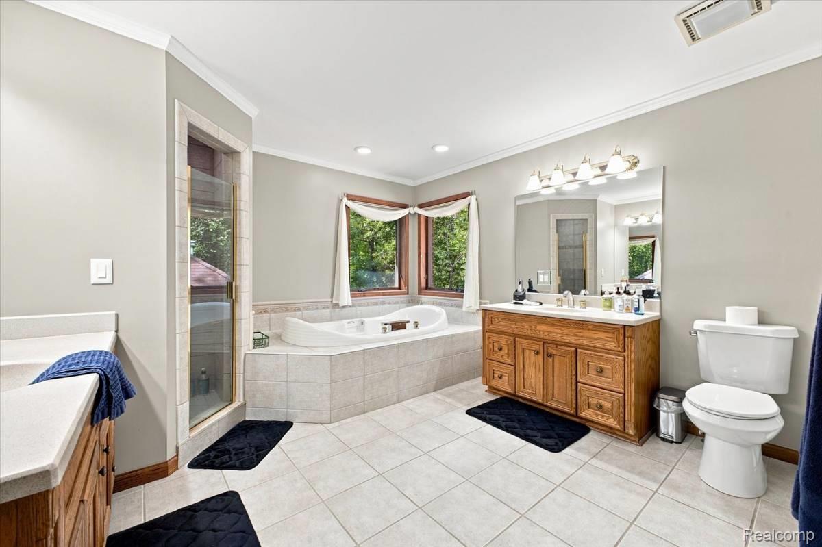 8610 Ferry Road Grosse Ile, MI 48138 - Photo 31 of 55 Tiled flooring leading to a built-in jetted bathtub, a glass-enclosed shower, and a wood-finish vanity with a large mirror and overhead lighting