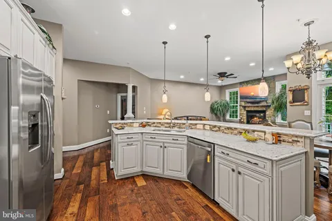 a kitchen filled with stainless steel appliances granite countertop a sink a stove a refrigerator and island with wooden floor
