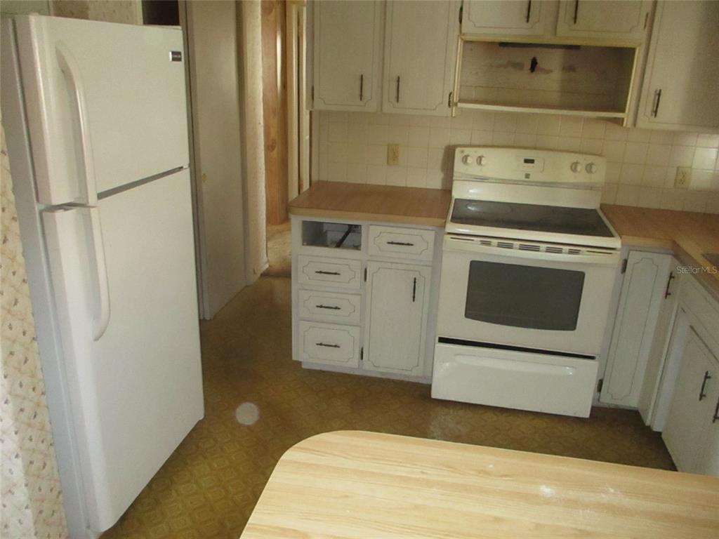 7403 Heather Street New Port Richey, FL 34653 - Photo 10 of 16 a kitchen with a refrigerator stove and white cabinets