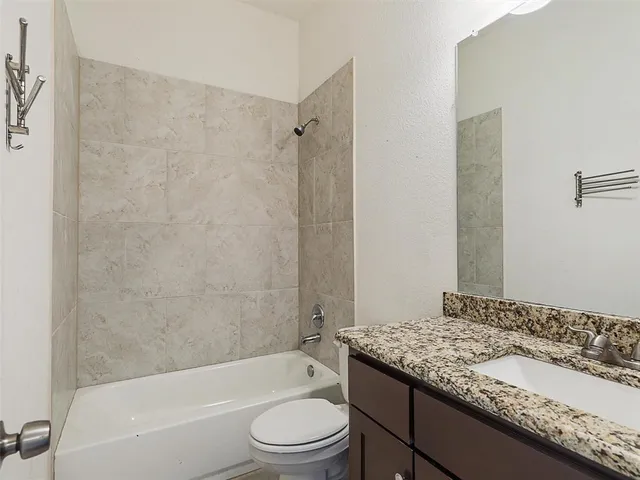 a bathroom with a granite countertop bathtub shower sink vanity mirror and toilet