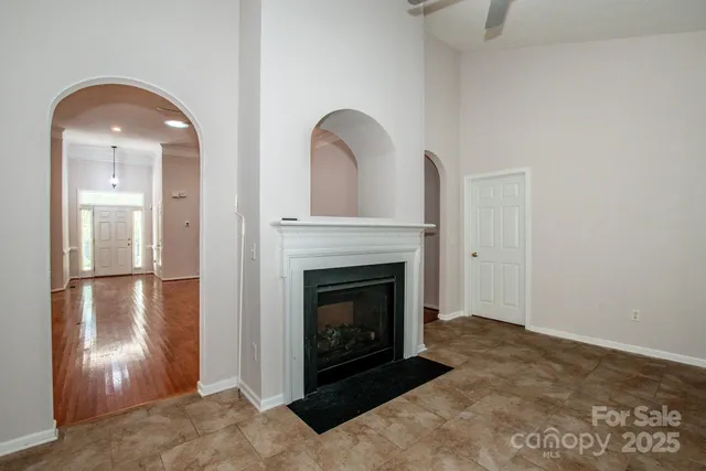 a view of an empty room with chandelier fan and fire place