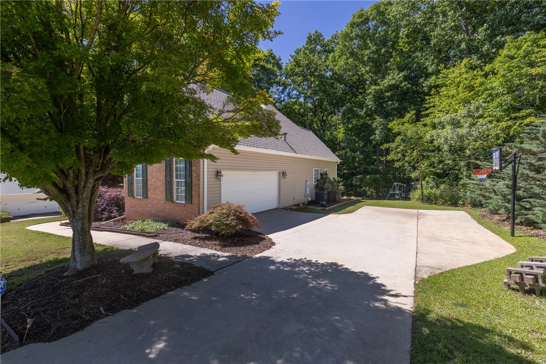 110 Brookstone Way Central, SC 29630 - Photo 38 of 46 This residence features a driveway leading to an attached garage, surrounded by lush trees and landscaping.