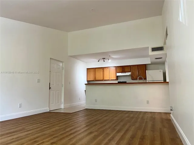 a view of kitchen and empty room with wooden floor