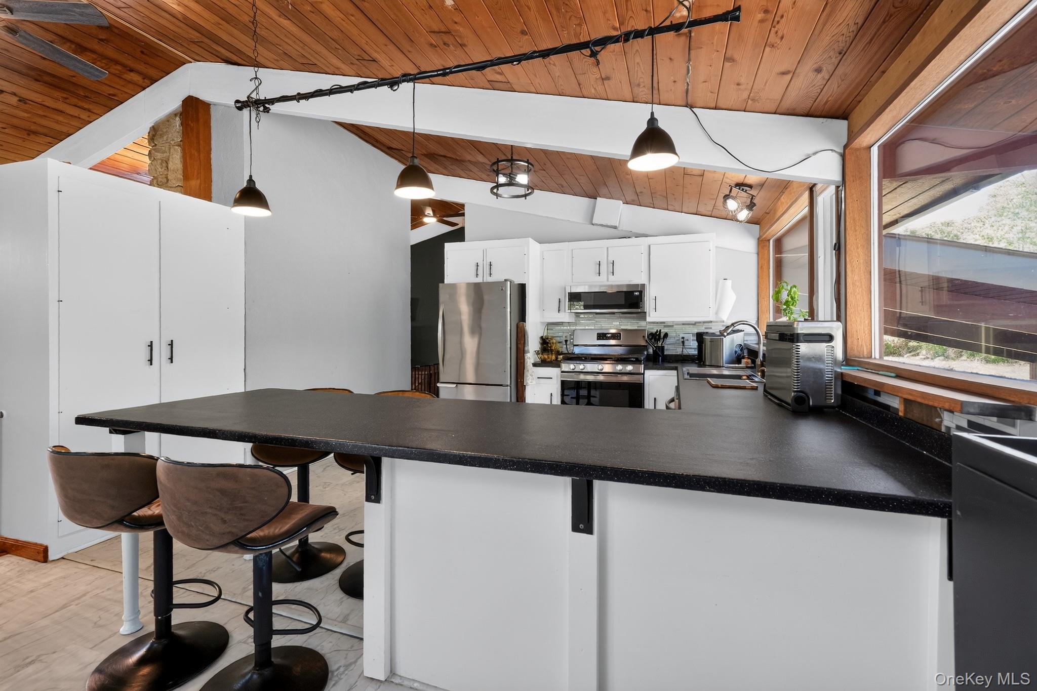 424 Laroe Road Chester, NY 10918 - Photo 31 of 43 Kitchen island with dark countertop, white cabinetry, stainless steel appliances, wood-finish vaulted ceiling, and integrated lighting fixtures
