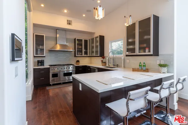 a kitchen with stainless steel appliances granite countertop a stove a sink dishwasher a oven a dining table and chairs with wooden floor