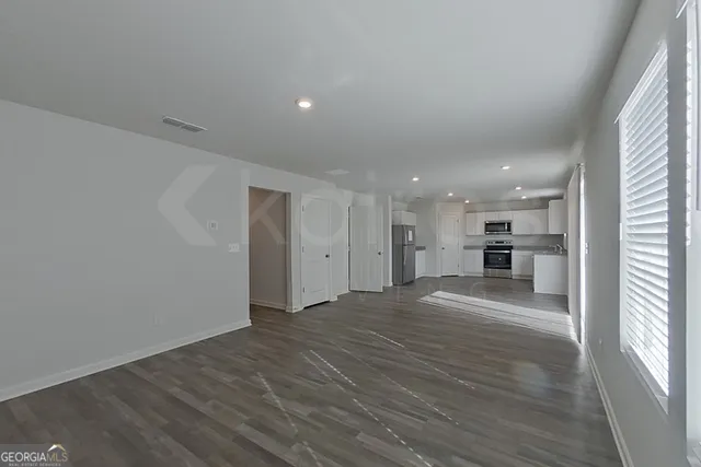 a view of empty room with wooden floor and kitchen
