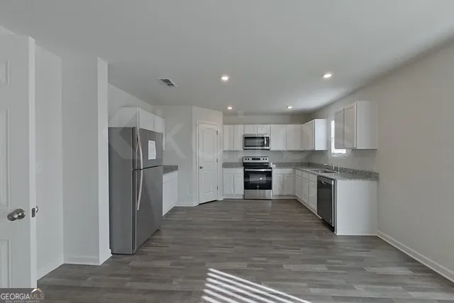 a view of a hallway with wooden floor and a refrigerator