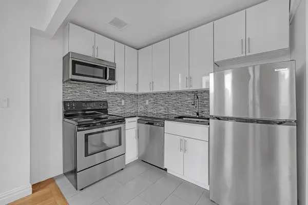 a white kitchen with stainless steel appliances granite countertop a refrigerator sink and white cabinets