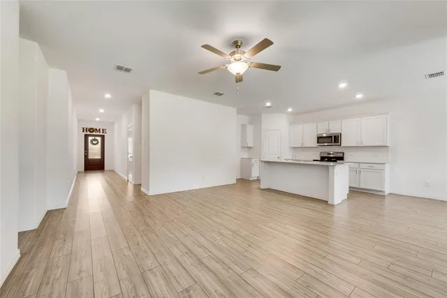 a view of an empty room and kitchen with wooden floor