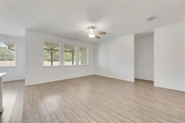 an empty room with wooden floor chandelier fan and windows