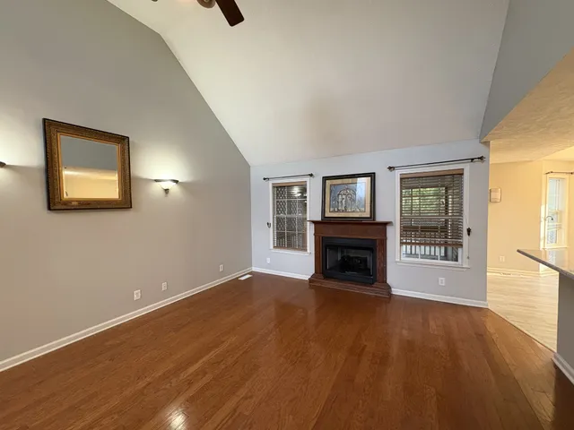 a view of an empty room with wooden floor fireplace and a window