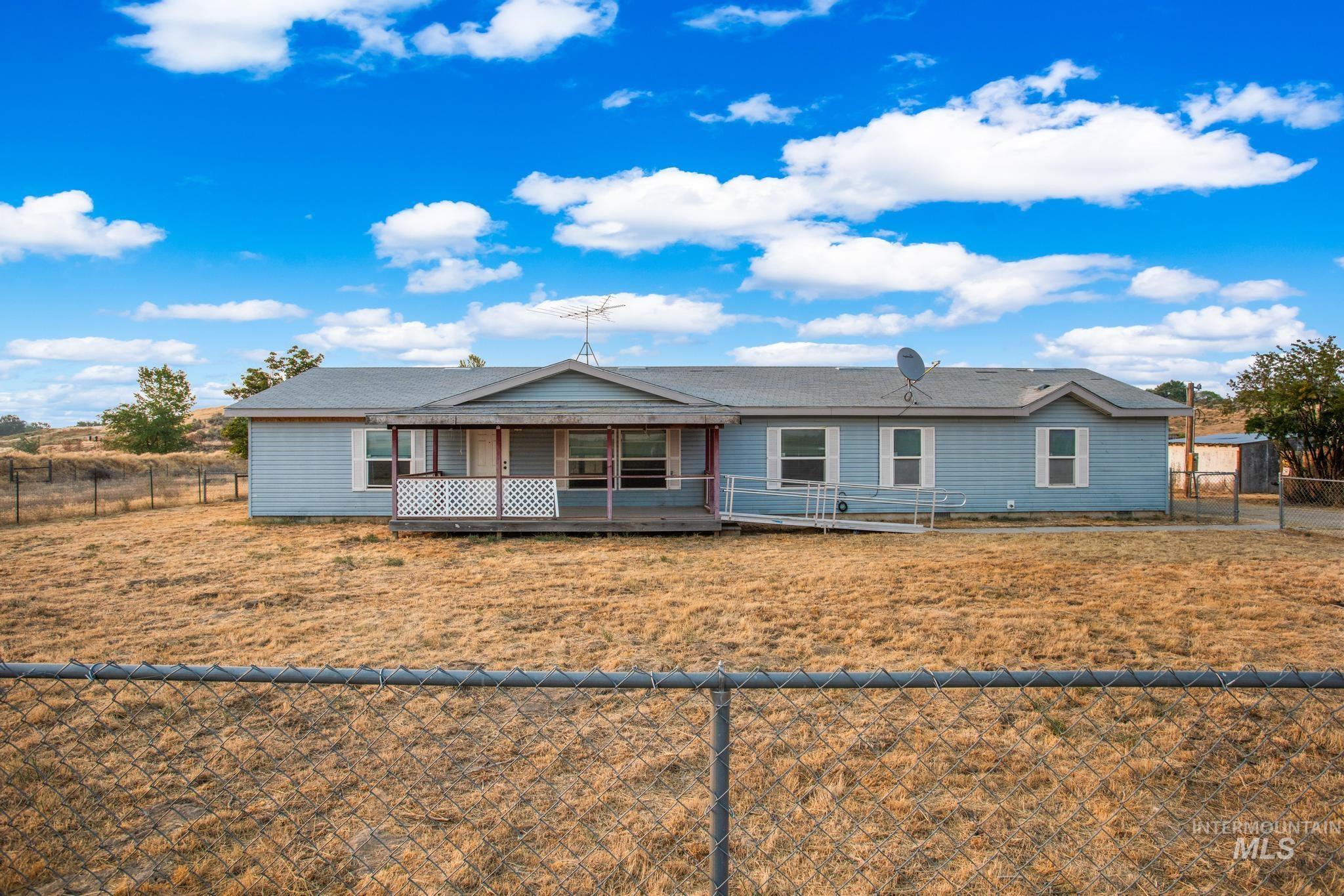 15190 Oasis Road Caldwell, ID 83607 - Photo 3 of 36 Light blue siding exterior with white window trim and shutters, featuring a covered front porch, a wheelchair ramp, and a chain-link fence