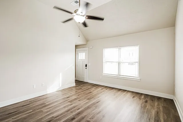 an empty room with wooden floor ceiling fan and windows