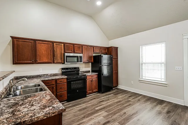 a kitchen with stainless steel appliances granite countertop a stove top oven a sink dishwasher a refrigerator and cabinets with wooden floor