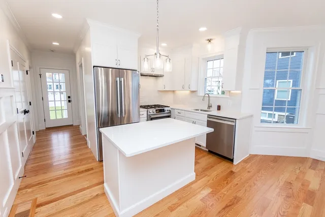 a kitchen with stainless steel appliances a stove a sink a refrigerator and white cabinets with wooden floor