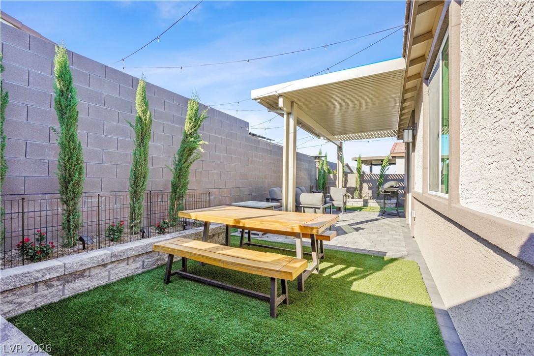 9398 Noble Fir Rdg Court Las Vegas, NV 89143 - Photo 28 of 36 A well-appointed patio with artificial turf, a shaded dining area, and string lights offers an inviting outdoor retreat.