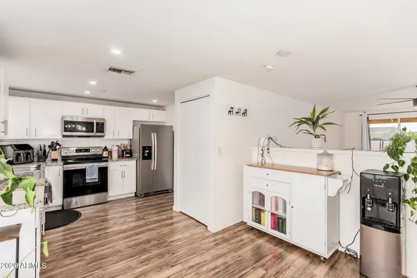 a kitchen with stainless steel appliances a white refrigerator a stove top oven a refrigerator and a dining table with wooden floor