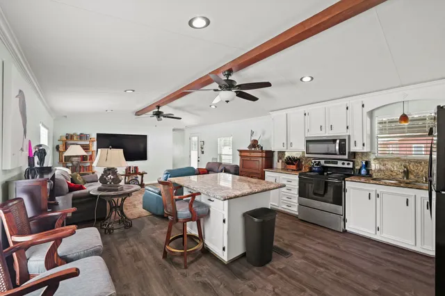 a open kitchen with stainless steel appliances kitchen island granite countertop a sink dishwasher a stove and a refrigerator with wooden floor