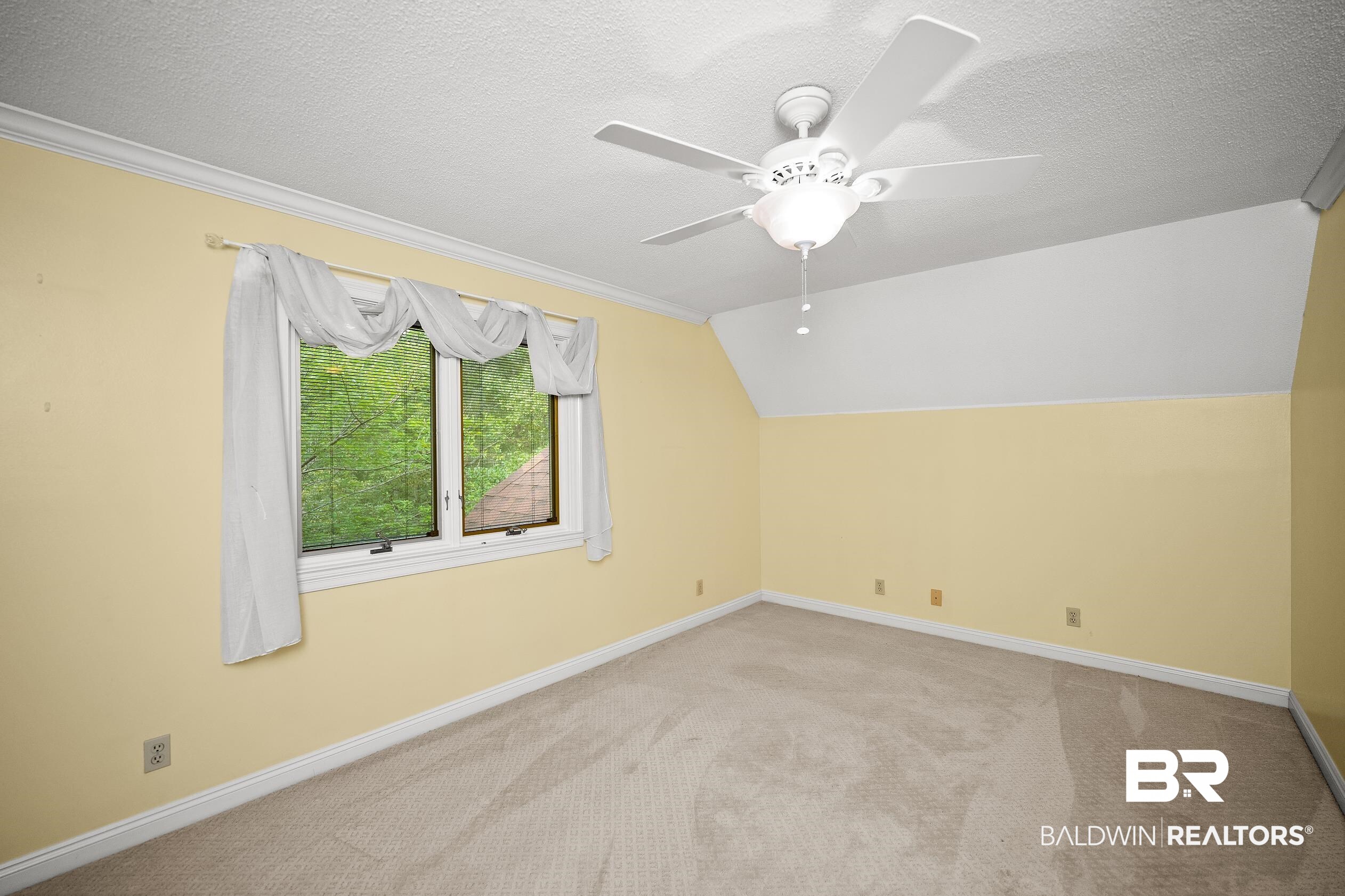 329 Norwood Road Monroeville, AL 36460 - Photo 30 of 49 Room featuring a window with exterior tree-line scenery, a white ceiling fan with integrated lighting, textured carpeting, crown molding, and a partial vaulted ceiling