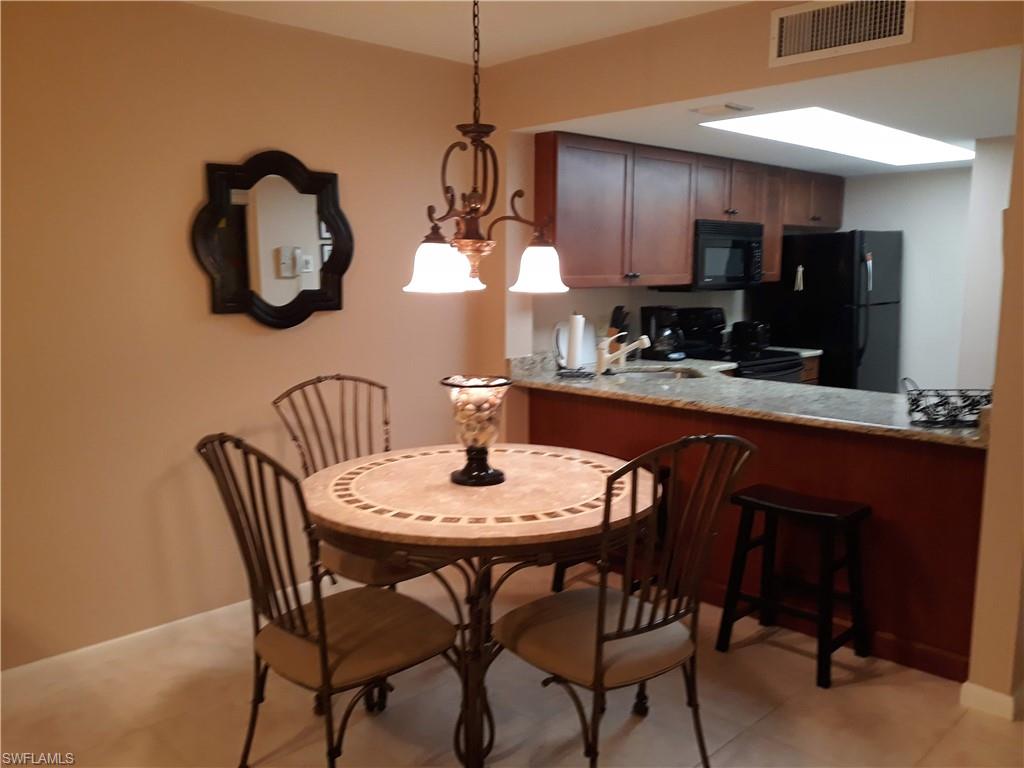 600 Neapolitan Way, Unit 147 Naples, FL 34103 - Photo 3 of 13 a dining room with wooden floor a chandelier a wooden table and chairs