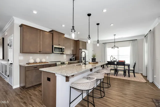 a kitchen with stainless steel appliances granite countertop a stove top oven a sink a dining table and chairs with wooden floor