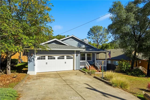 a view of a white house with a large tree and couches chairs under an umbrella