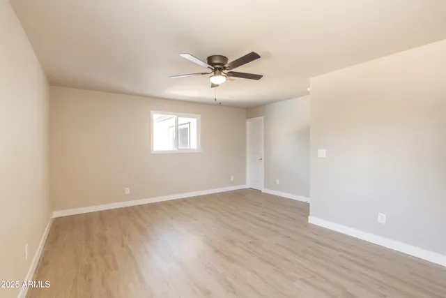 an empty room with wooden floor ceiling fan and windows