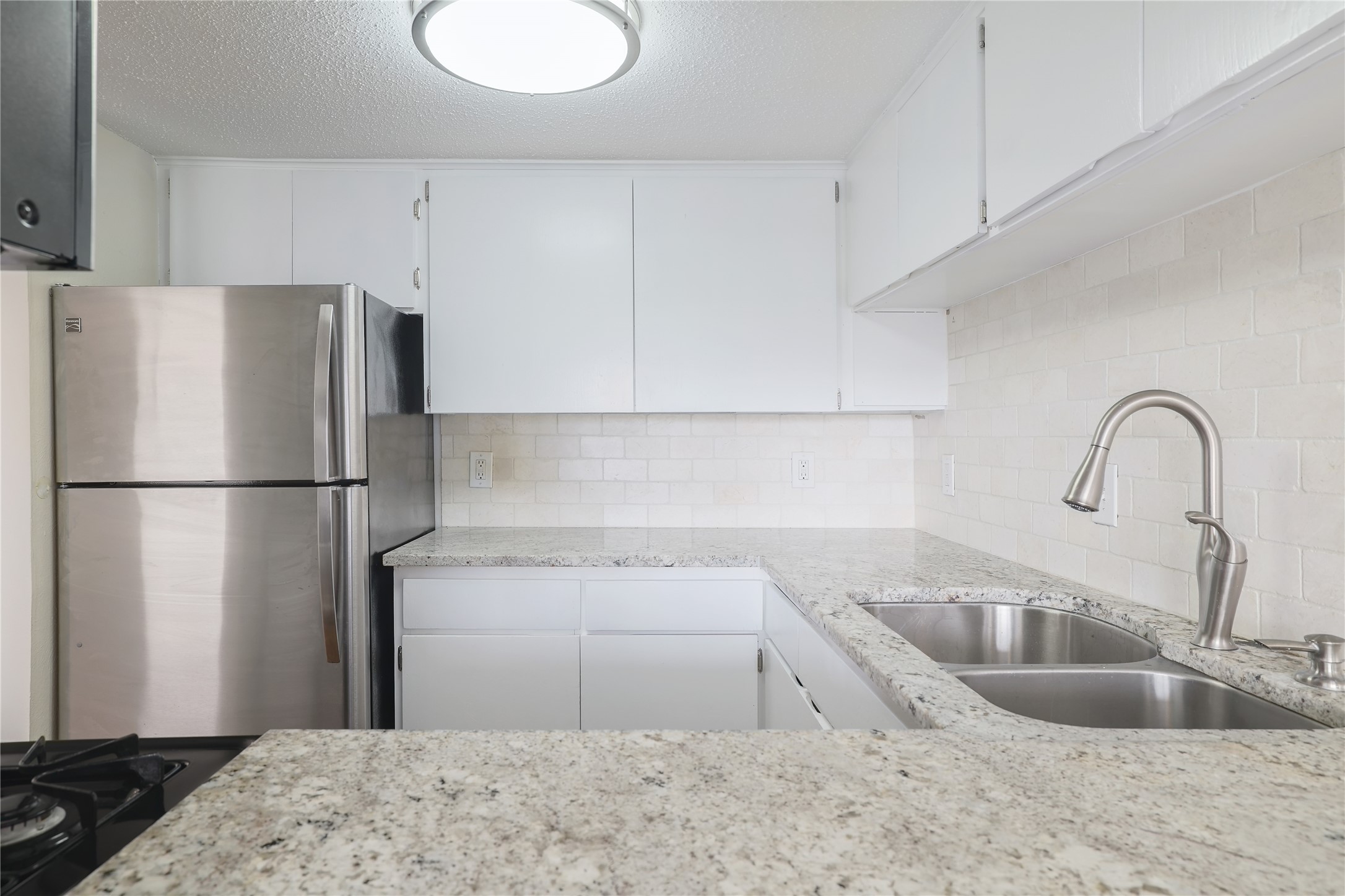 1800 Lavaca Street, Unit A508 Austin, TX 78701 - Photo 17 of 25 The kitchen features white cabinetry, granite countertops, a stainless steel refrigerator, and a double basin sink with a brushed nickel faucet