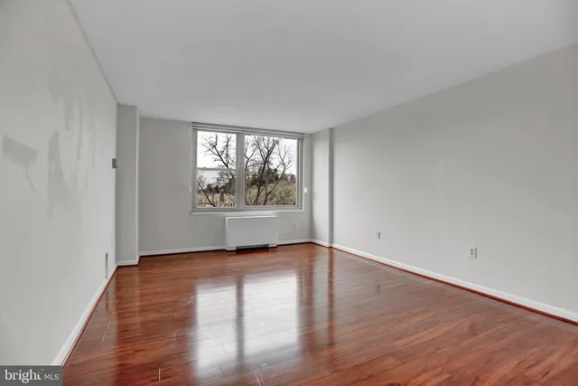 a view of an empty room with wooden floor and a window