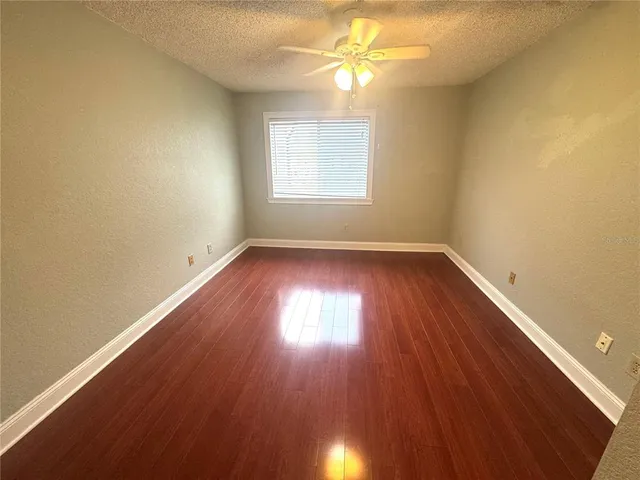 an empty room with wooden floor chandelier fan and windows