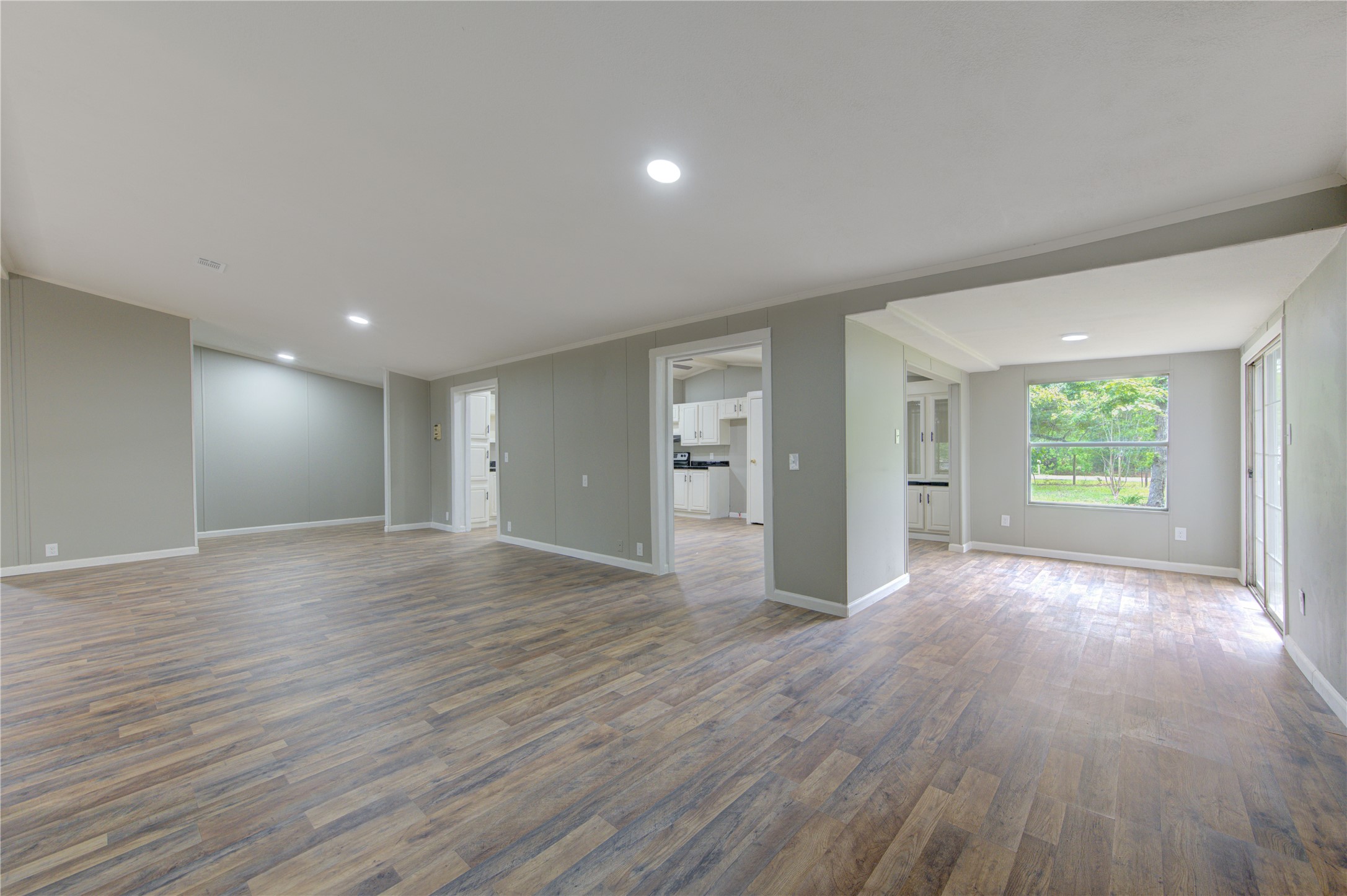 30226 Davis Street Magnolia, TX 77355 - Photo 11 of 50 This photo showcases a spacious, open-concept living area with wood-style flooring and neutral walls. It features large windows that allow plenty of natural light, and a modern kitchen in the background. Ideal for flexible living and entertaining.