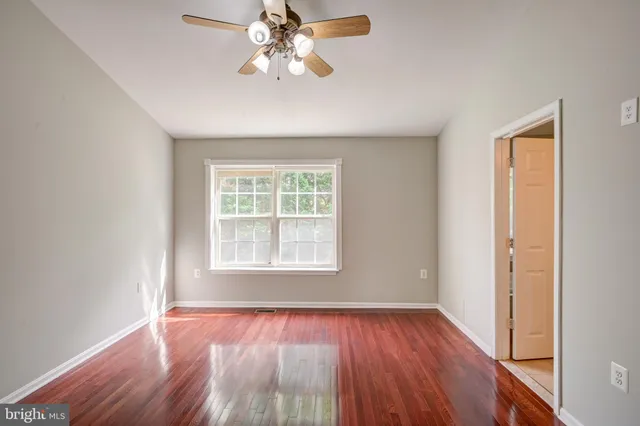 an empty room with wooden floor chandelier fan and windows