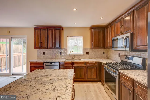 a kitchen with stainless steel appliances granite countertop a stove top oven a sink dishwasher a dining table and chairs with wooden floor