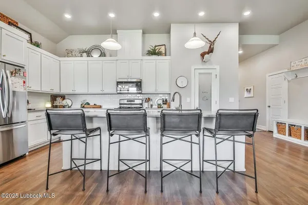 a kitchen with stainless steel appliances kitchen island granite countertop a refrigerator a stove a sink and chairs with wooden floor