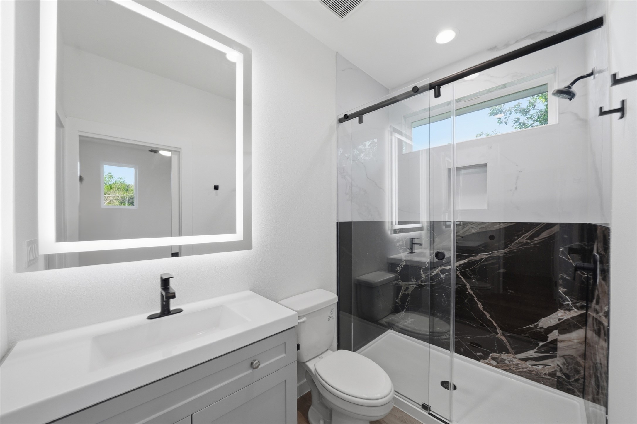 2212 Yellow Jacket Lane, Unit 2 Austin, TX 78741 - Photo 20 of 25 Contemporary bathroom featuring a frameless glass shower enclosure with sliding door, a vanity with a white countertop and integrated sink, a rectangular backlit mirror, and a wall-mounted showerhead with matching fixtures