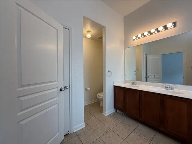 a spacious bathroom with a double vanity sink a toilet and a mirror
