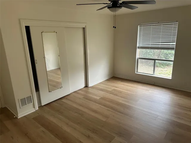 an empty room with wooden floor fan and windows