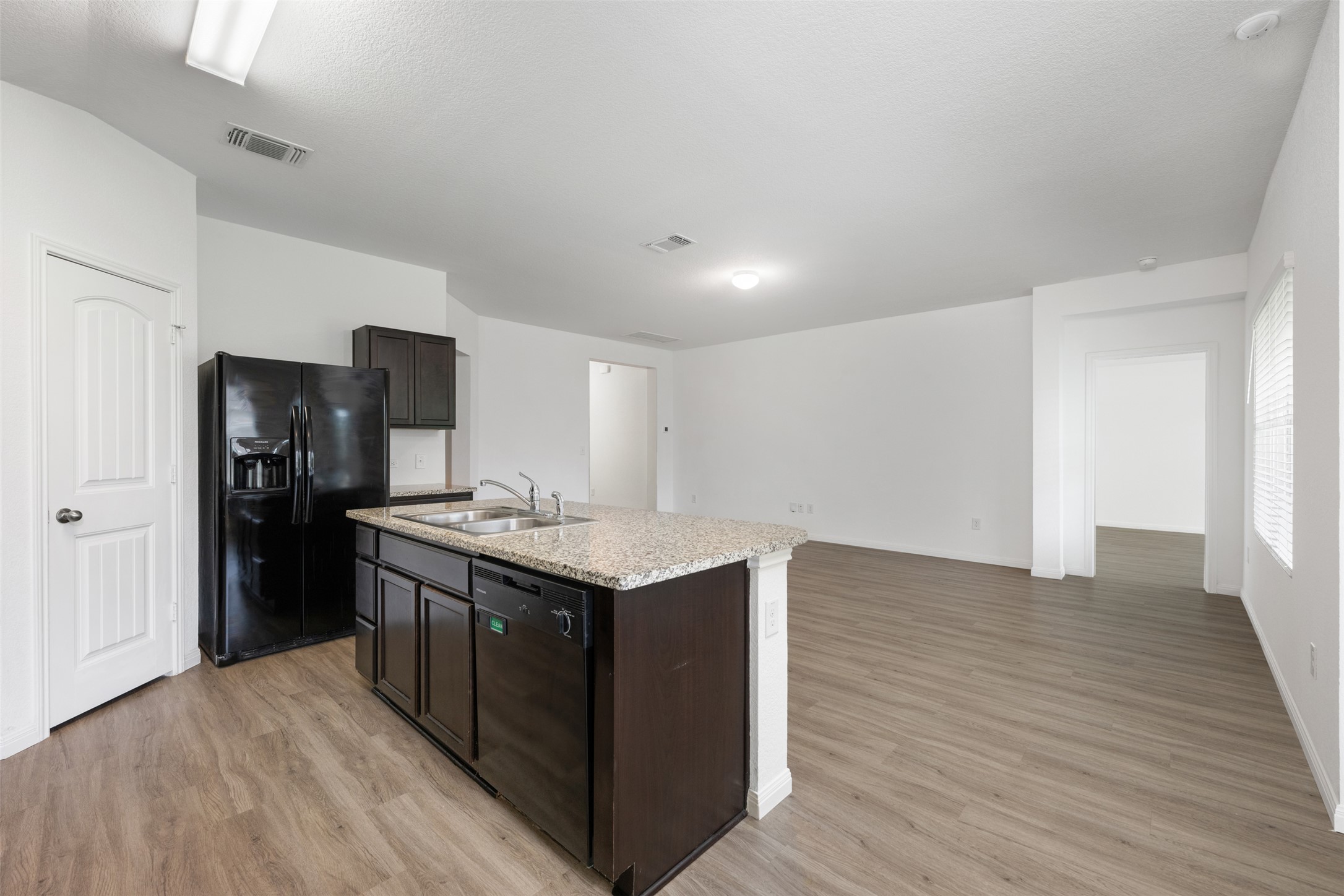 14900 Retha Pass Austin, TX 78725 - Photo 12 of 39 Open-concept kitchen featuring an island with granite-style countertops, integrated double basin sink, dishwasher, dark wood cabinetry, and wood-finish flooring