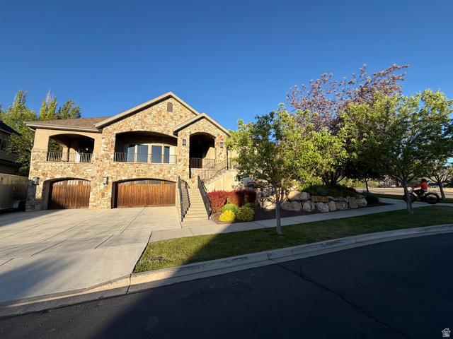 Stone exterior residence featuring two wood-finish garage doors, a concrete driveway, and an upper-level balcony