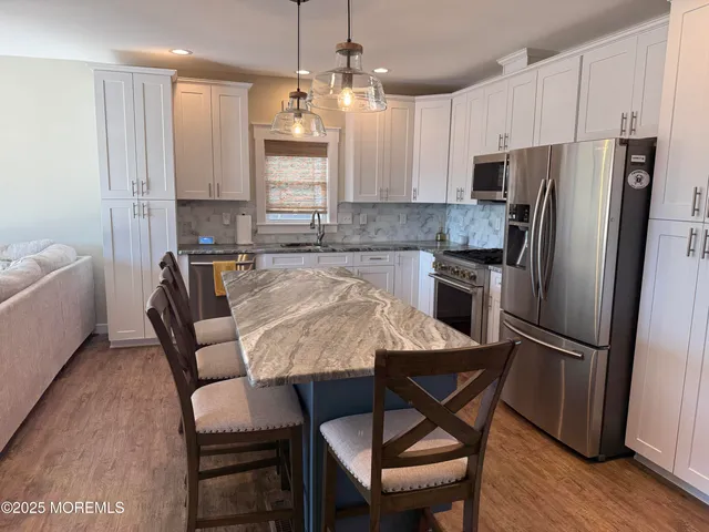 a kitchen with stainless steel appliances granite countertop a dining table chairs refrigerator and microwave