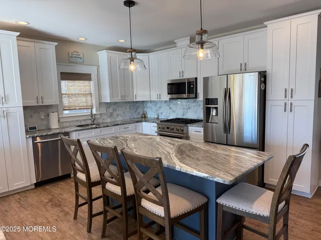 a kitchen with stainless steel appliances granite countertop a sink a stove a refrigerator a dining table and chairs