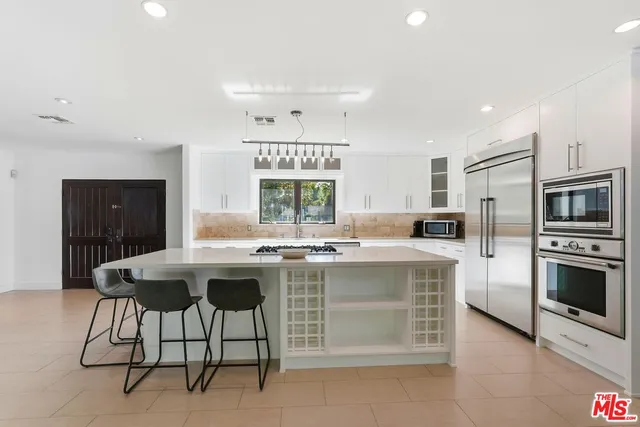 a kitchen with kitchen island stainless steel appliances a table chairs sink and cabinets