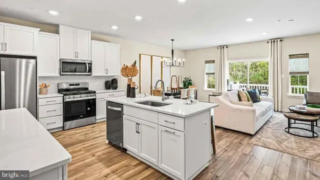 a kitchen with stainless steel appliances granite countertop a stove top oven a refrigerator a sink and white cabinets with wooden floor