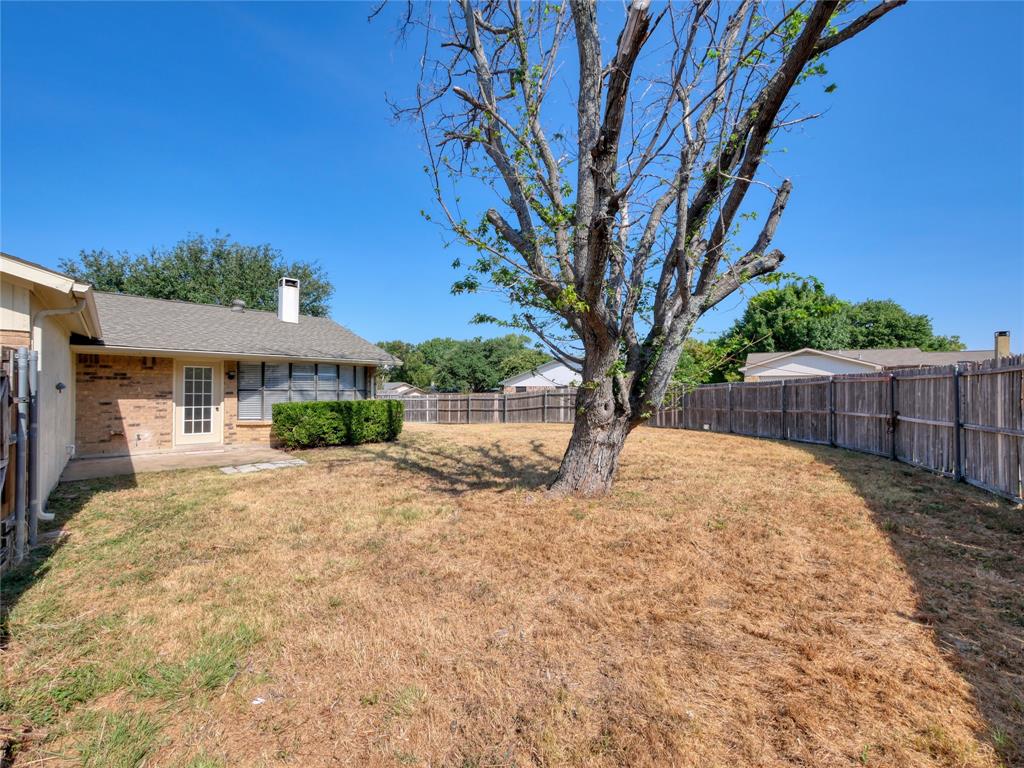1472 Rockshire Drive Plano, TX 75074 - Photo 24 of 27 Expansive backyard featuring a mature tree, privacy fencing, and a brick-faced exterior with a patio