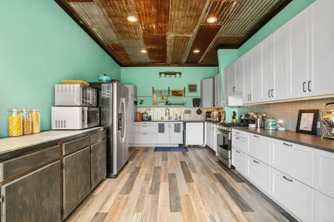 a kitchen with granite countertop a refrigerator a sink dishwasher a stove and white cabinets with wooden floor