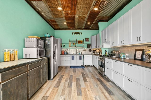 a kitchen with granite countertop a refrigerator a sink dishwasher a stove and white cabinets with wooden floor