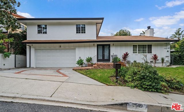 a view of a white house with small yard plants and a large tree